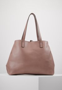 Sac fourre-tout en cuir doux couleur rose pâle avec une texture lisse ; doté de longues poignées et d'un accent noir subtil le long des bords.