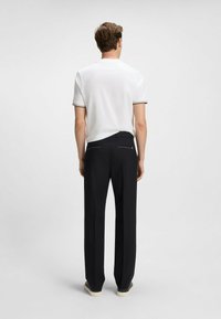 White polo shirt with black trim paired with black trousers. Trousers feature a tailored fit and back pockets with subtle detailing.