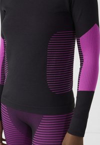 Top deportivo negro con detalles en rayas rosas en las mangas y el cuerpo. Detalle texturizado en tonos contrastantes. Diseño ajustado que complementa la ropa deportiva.