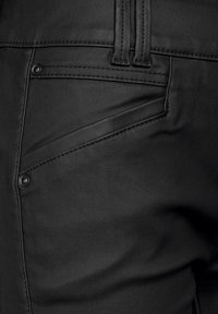 Mustat nahkahousut, joissa on sileä pinta, kaksi taskua ja tarkat tikkaukset saumoissa, tiukasti istuva muotoilu.