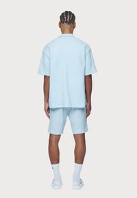 Vaaleansininen, teksturoitu lyhythihainen paita ja siihen sopivat shortsit. Rentoa mallia, kauluksellinen. Yhdistetty valkoisiin sukkiin ja kenkiin.