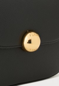 Superficie in pelle nera a granuli con bottone rotondo dorato inciso con la scritta "FURLA" su una borsa o un accessorio.