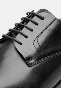 Schwarze Lederschuhe mit glatter Textur, runder Spitze und vier Ösen für das Schnürsystem. Verfügt über kontrastierende Nähte entlang der Nähte.