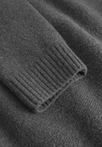 Dettaglio di un maglione di lana grigio con polsini a coste e una superficie morbida e testurizzata, che mostra un motivo di maglia liscio e uniforme.