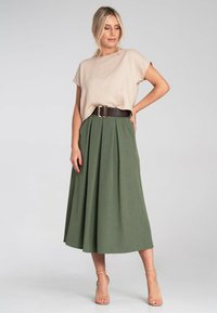 Beżowy top z krótkim rękawem i zielona plisowana spódnica midi, trzymana szerokim brązowym paskiem. Modelka w cielistych szpilkach na neutralnym tle.