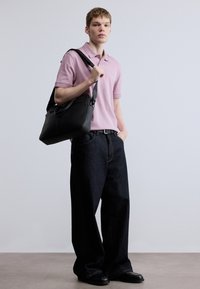 Črna usnjena torbica čez ramo, svetlo roza polo majica, temno modre široke kavbojke, črne čevlje z okroglim nosom, minimalistični dodatki, enostavno ozadje.