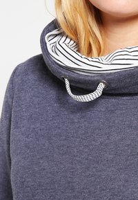 Sudadera navy con cuello alto y un interior a rayas. Presenta un cordón y una tela suave y texturizada.