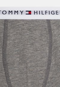 Graue Baumwoll-Boxershorts mit einem weißen elastischen Bund, der das "TOMMY HILFIGER"-Logo in Schwarz und Rot aufweist. Glatte Textur mit kontrastierenden Nähten.