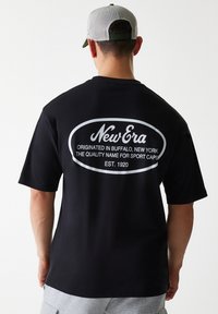 Black T-shirt made of cotton, featuring a large white text print on the back that reads "New Era," with an oval outline and additional text below.