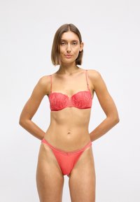 Conjunto de lingerie coral composto por um sutiã com aro de renda e uma cueca a condizer. O sutiã possui alças ajustáveis e detalhes de bordado floral.
