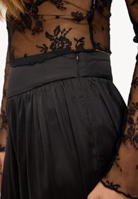 Haut en maille noire avec un motif en dentelle florale, associé à une jupe en satin noir ajustée ornée de plis et d'une fermeture éclair discrète.