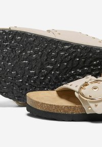 Sandali beige con cinturino borchiato, soletta in sughero e suola in gomma nera testurizzata. Presentano un dettaglio con fibbia metallica circolare.