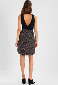 Musta hihaton paita syvällä V-mallisella selkäosalla, yhdistetty polvipituiseen hameeseen, jossa on vaaleanpunainen ja valkoinen kukkakuvio mustalla pohjalla.