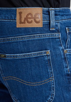 Primo piano della tasca posteriore e della cintura di jeans di denim blu con etichetta in pelle marrone del marchio Lee cucita sopra la tasca.