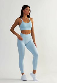 Jasnoniebieski zestaw sportowy składający się z dopasowanego stanika sportowego z cienkimi ramiączkami oraz legginsów z wysokim stanem, oba o prążkowanej fakturze. Białe sneakersy.