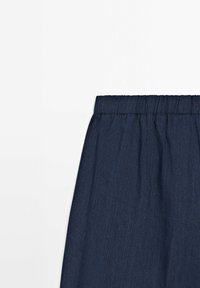 Section de jupe en denim bleu foncé avec une taille élastique sur fond blanc.
