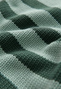 Coperta lavorata a maglia con motivi a diamante alternati in verde chiaro e verde scuro. La texture appare morbida e accogliente con una lavorazione multi-dimensionale.