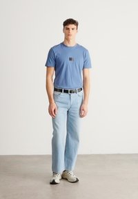 Světle modré bavlněné tričko s malou tmavou nášivkou loga, kombinované se světle modrými džínovými kalhotami a šedými teniskami. Jednoduchý, neformální design.