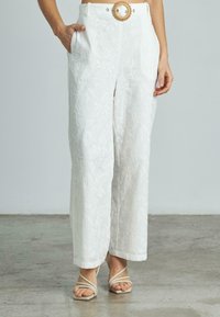 Weiße bestickte Hose mit floralem Muster, weit geschnitten, mit Seitentaschen und einem der chunky gewebten Gürtel-Detail.