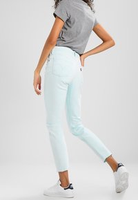 Vaqueros de mezclilla azul claro con cintura alta y pierna recta, con un dobladillo ligeramente deshilachado, combinados con una camiseta gris y zapatillas blancas.