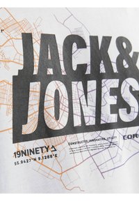 Camiseta gráfica en blanco con el nombre en negrita "JACK & JONES" en negro. Presenta patrones de mapa en naranja y púrpura. Detalle de impresión texturizada.