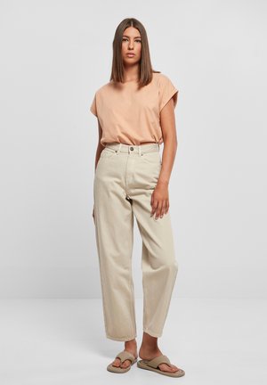 Lys ferskenfarvet kortærmet t-shirt kombineret med beige brede bukser og beige sandaler. Stoffet ser blødt ud med en afslappet pasform.