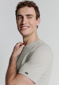 Grijze t-shirt met korte mouwen, gemaakt van zachte stof, met een ronde halslijn en een klein merklabel op de linkermouw.