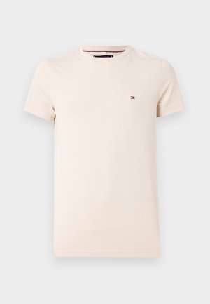 T-shirt en coton beige avec un col ras du cou et des manches courtes, arborant un petit logo sur la poitrine gauche. Texture lisse, coupe classique.
