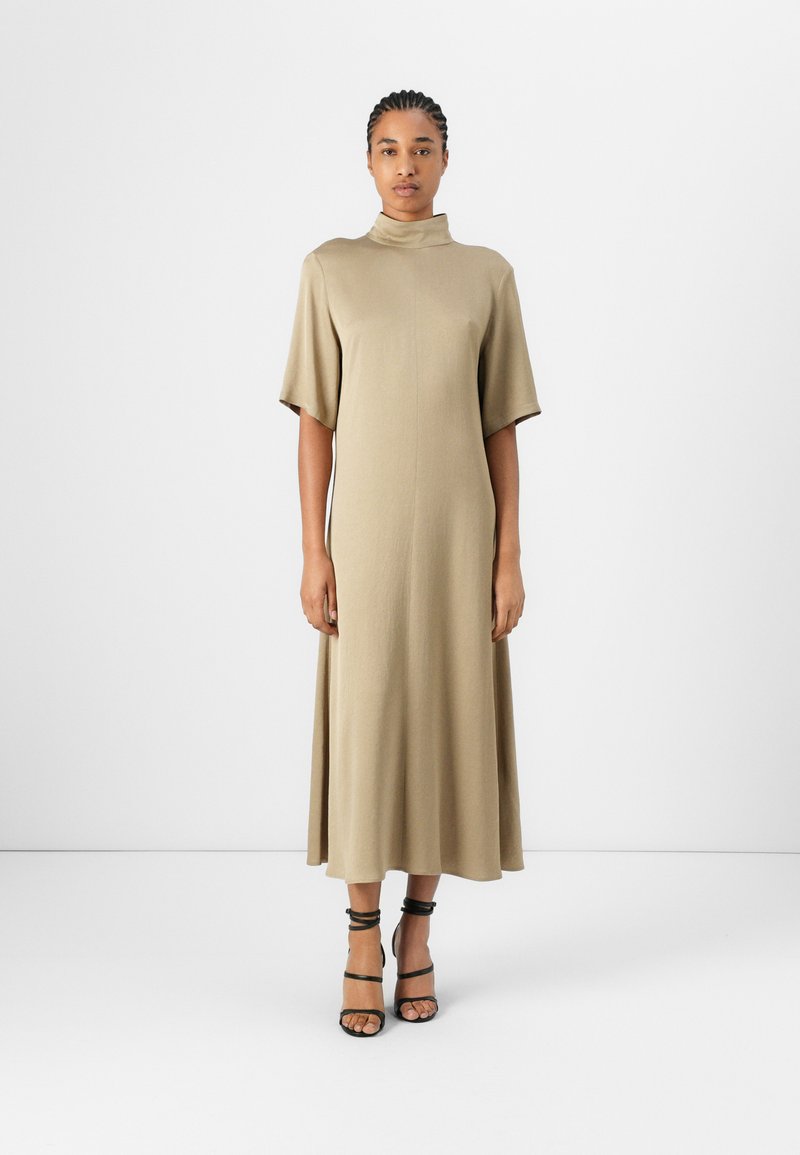 Khaki midi ruha rövid ujjakkal és magas nyakkal, puha anyagból készült. Fekete pántos magassarkúkkal van párosítva. Egyszerű, minimalista dizájn.