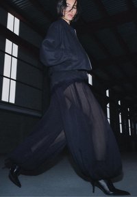 Jachetă bomber neagră cu mâneci largi, purtată peste o fustă neagră transparentă. Ținuta are un design fluid și este completată de cizme negre cu toc înalt.