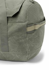 Groene gewaxte stoffen sporttas met verstevigde handvatten en een zijhandgreep op een witte achtergrond.