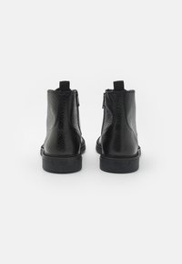 Botas de tobillo de cuero negro con un acabado texturizado, cierre de cremallera en el lateral y una suela robusta de goma negra.