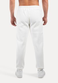 Pantalones de chándal blancos con cintura elástica y piernas ajustadas, que presentan una textura suave y un detalle de costura mínimo, combinados con zapatillas blancas.