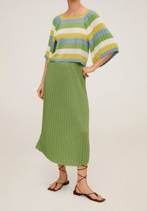 Gestreepte top in blauw, groen, geel en wit; cropped ontwerp met brede mouwen. Lange, geplooide groene rok. Bruine sandalen met bandjes.