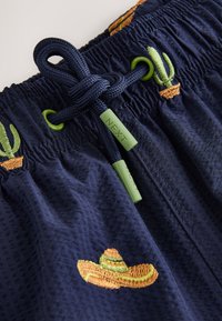 Short bleu marine avec taille élastique et cordon, orné de broderies de cactus verts et de sombrero marron.