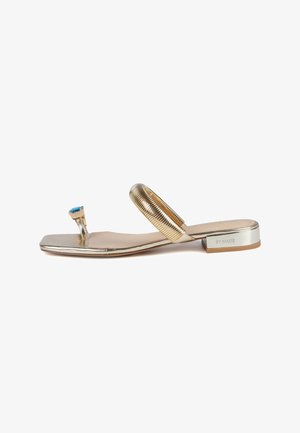 Metallic gold flat sandal featuring a square toe, a textured strap, and a decorative blue stone on the front. Brand name is on the heel.