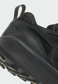 Scarpa da ginnastica nera con tomaia in mesh testurizzato, suola in gomma con profonde scanalature e linguetta rinforzata sul tallone per supporto.