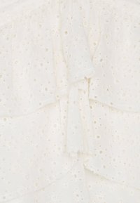 Tessuto bianco con una superficie testurizzata caratterizzata da intricati motivi ad occhio e rouches stratificati. Materiale morbido, leggero e traspirante.