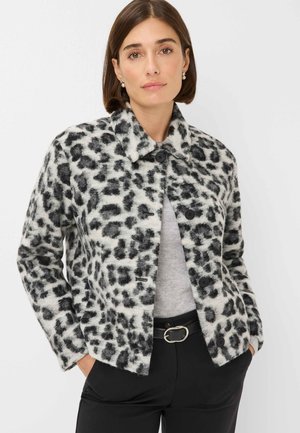 Jasje met luipaardprint van zachte stof, met een zwart-wit patroon, een kraag en twee knopen. Gecombineerd met een grijze top en zwarte broek.