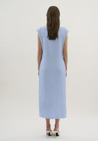Rochie de culoare albastru deschis, până la genunchi, dintr-un material texturat, cu mâneci scurte, croi drept și un model subtil, asortată cu pantofi cu toc și spatele descoperit.