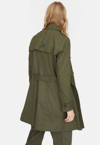 Olijfgroene trenchcoat met een achtercape en knoopdetails, voorzien van een ceintuurlijn en opgerolde mouwen, gemaakt van lichtgewicht stof.