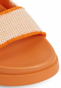 Mules orange avec un dessus à motif à carreaux blancs et orange, bords de sangle texturés et une semelle lisse et robuste.