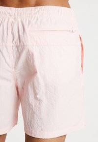 Pantaloni shorts rosa chiaro realizzati in un tessuto morbido, dotati di una cintura elastica, tasche laterali e una tasca posteriore con zip per un sicuro riporre.