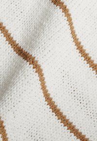 Valkoinen viltti, jossa on teksturoitu neulottu kuvio, vaakasuorat ruskeat raidat ja siksak-ompeleet lisäyksinä.