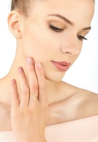 Gold ring featuring a 'V' design and small clear gemstone accent. Model's hand rests on her face, showcasing the ring's details.