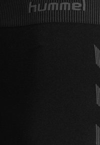 Leggings de sport noirs avec une taille texturée arborant le logo "hummel", un tissu lisse et un motif à rayures diagonales dans une teinte plus claire.