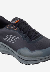 Zapatilla deportiva negra con un upper de malla texturizada y acentos grises, una suela acolchada y detalles reflectantes. Marca en la lengüeta.