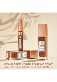 Trois produits de maquillage présentés : un sérum teinté, un correcteur et un fond de teint. Tous ont un emballage en verre et métallique dans des teintes de marron et d'or rose.