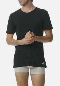 Camiseta de algodón negra con cuello redondo, mangas cortas y un pequeño logotipo blanco en el lado inferior, combinada con pantalones cortos grises.