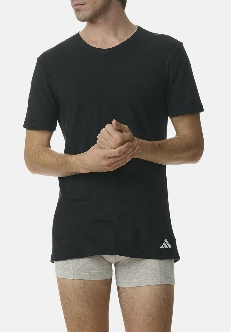 Camiseta de algodón negra con cuello redondo, mangas cortas y un pequeño logotipo blanco en el lado inferior, combinada con pantalones cortos grises.